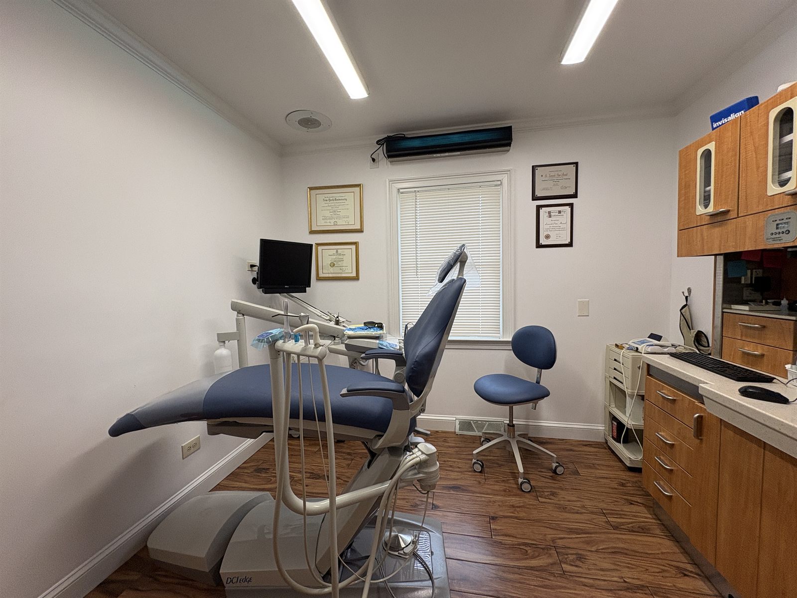 Treatment room at Stratford Dental Care with a dental chair, overhead light, and framed diplomas